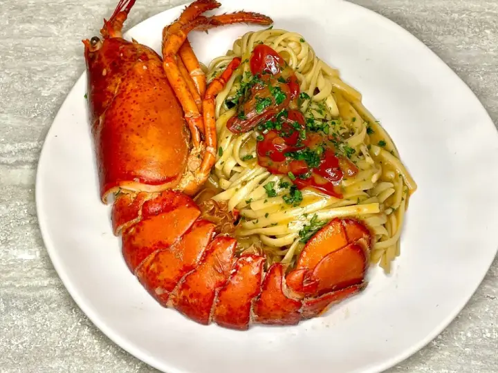 Un piatto di linguine all'astice, con pasta condita e astice intero, guarnito con pomodorini e prezzemolo.