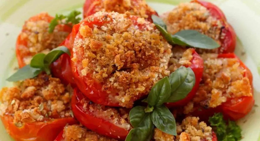 Pomodori al forno ripieni di pangrattato e erbe aromatiche, guarniti con basilico fresco.