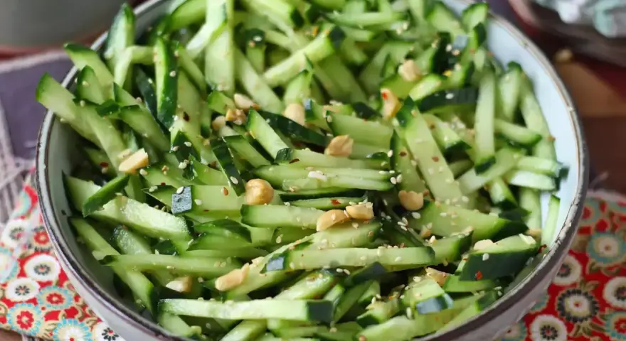 Una ciotola piena di fresca insalata di cetrioli tagliati a julienne, condita con semi di sesamo e arachidi croccanti.