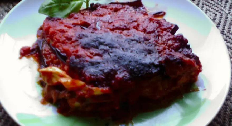 Una porzione di parmigiana di melanzane napoletana, ricca e saporita, guarnita con basilico fresco.