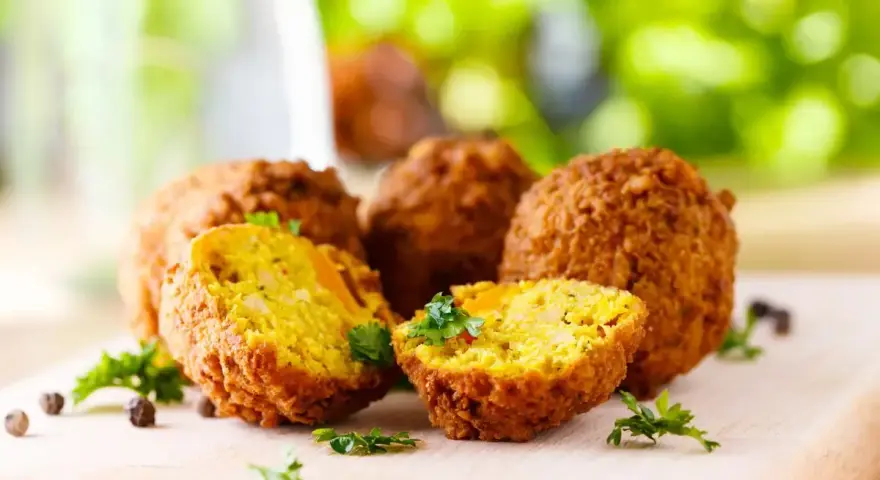 Polpette di ceci dorate e croccanti, cotte in friggitrice ad aria, guarnite con prezzemolo fresco su tagliere di legno.