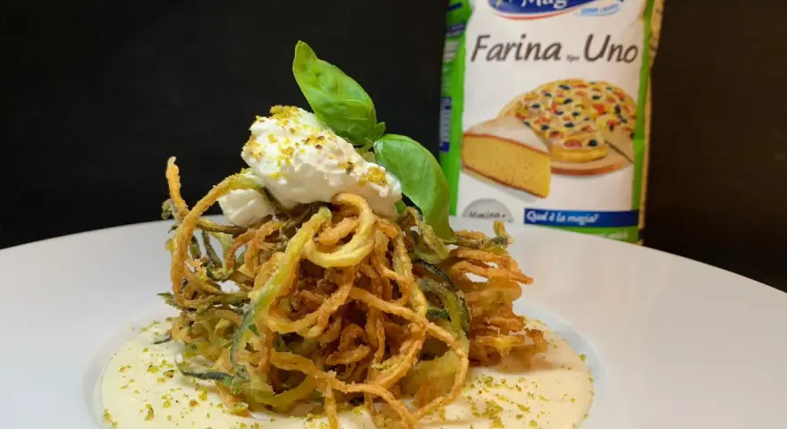 Deliziosi spaghetti di zucchine fritte croccanti, serviti su una crema vellutata e guarniti con ricotta fresca e basilico.