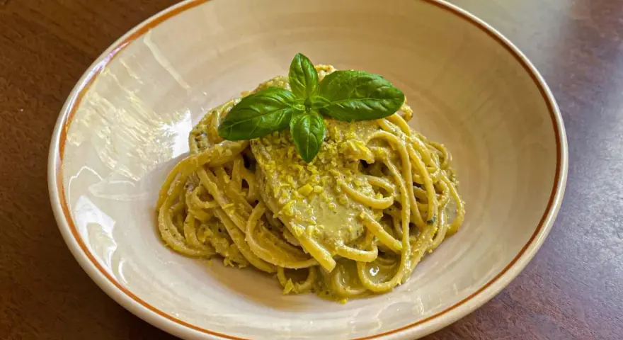 Spaghetti conditi con un cremoso pesto di limone, guarniti con basilico fresco. Una deliziosa ricetta per un primo piatto estivo.