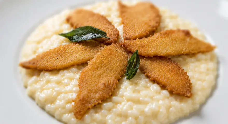 Un cremoso risotto al pesce persico, guarnito con filetti dorati e foglie di salvia croccante, un piatto che invita alla degustazione.