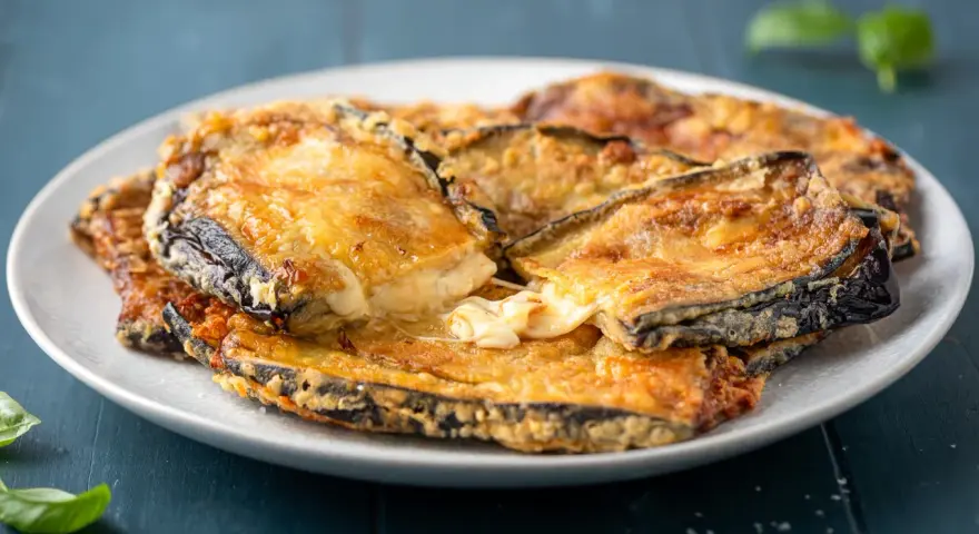 Melanzane contorno dorate e filanti, un piatto invitante con formaggio fuso e basilico fresco.