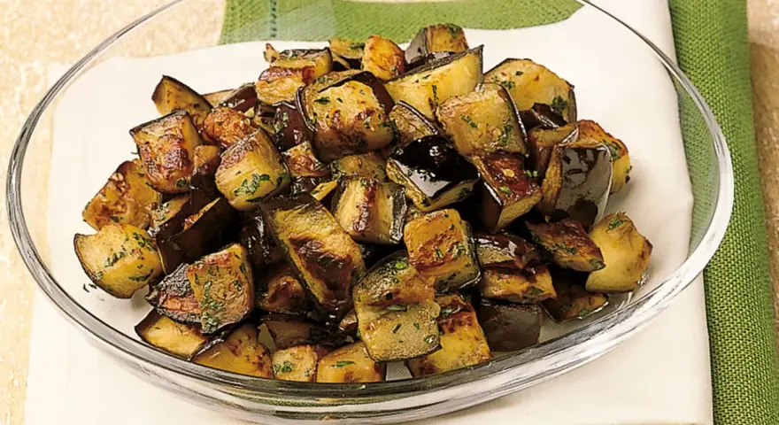Melanzane a funghetto ricetta della nonna: cubetti dorati e saporiti, conditi con erbe aromatiche, in una ciotola di vetro.