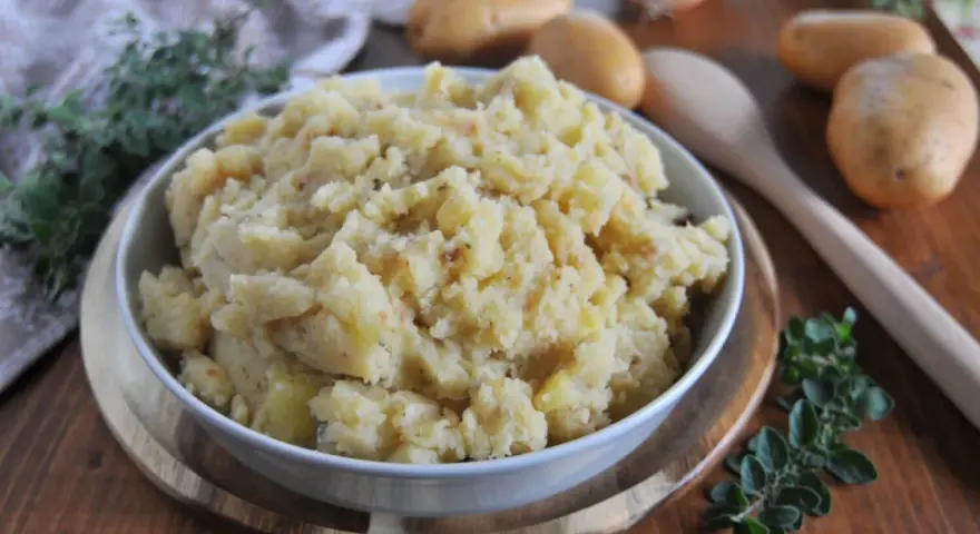 Un saporito piatto di patate in tecia, cotte con erbe aromatiche e spezie, servite in una ciotola su un tagliere di legno.