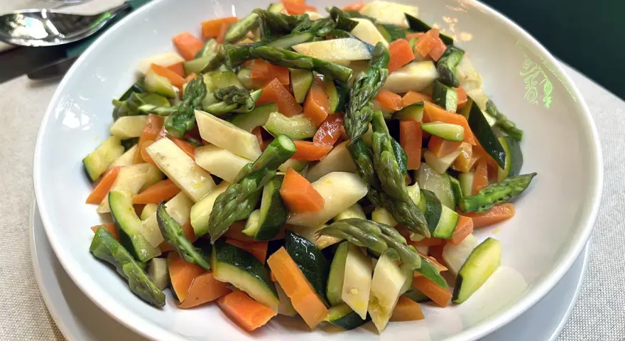 Un piatto invitante di verdure in padella: asparagi, carote e zucchine tagliate a pezzetti, condite con un filo d'olio.