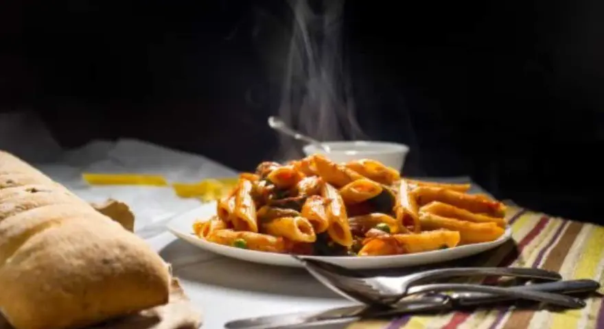 Piatto fumante di penne alla vodka, con pane croccante e posate pronte per gustare questo classico italiano.
