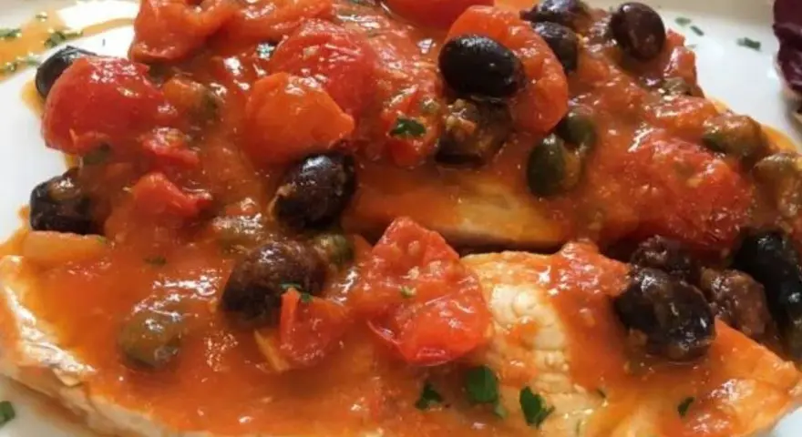 Delizioso pesce spada al forno con pomodorini, olive nere e capperi, un piatto saporito e colorato.