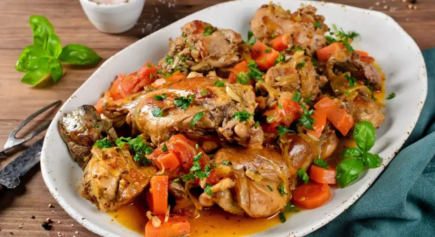 Un saporito coniglio in umido con carote e erbe aromatiche, servito su un piatto bianco.