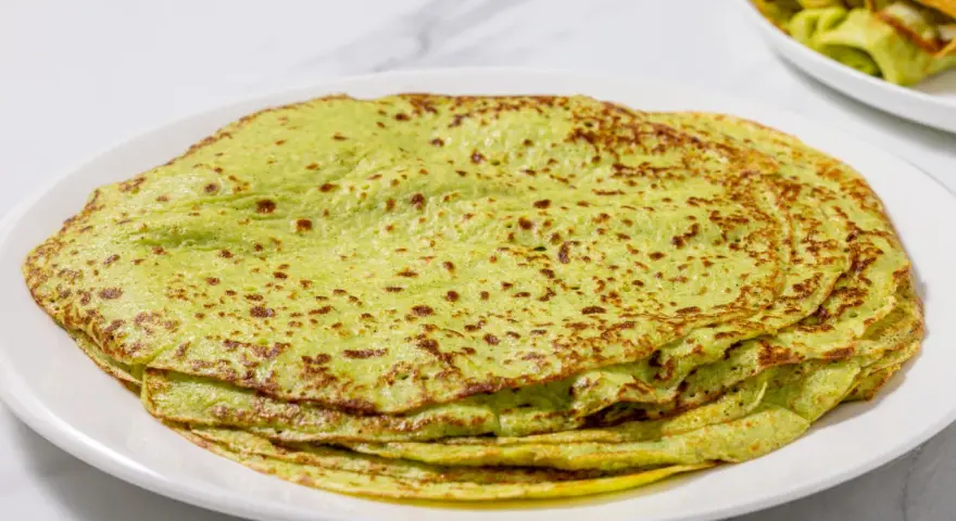 Piatto di crepes di zucchine verdi, sottili e leggermente dorate, impilate su un piatto bianco.