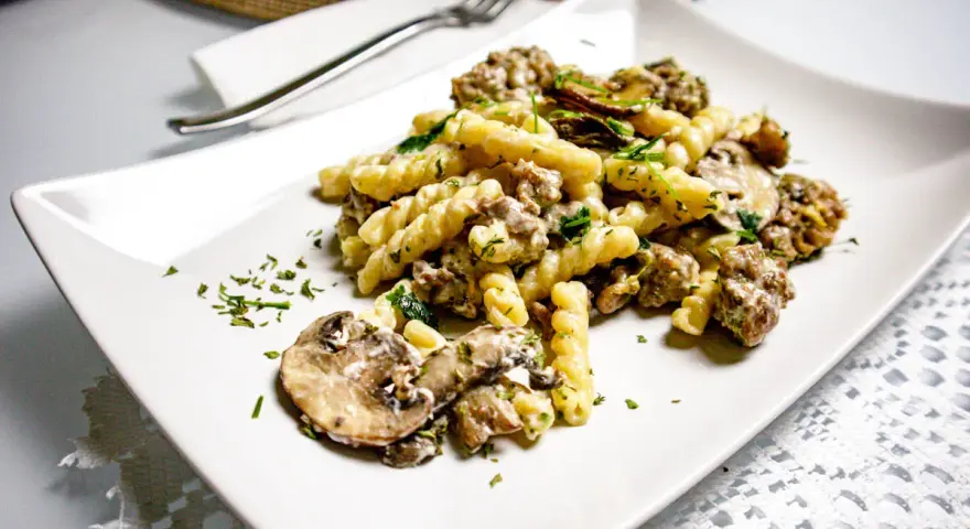 Un piatto di pasta salsiccia e funghi, condito con prezzemolo fresco, servito su un piatto bianco.