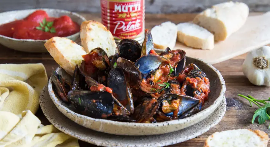 Piatto fumante di cozze alla tarantina ricetta, con pane tostato e pomodori pelati Mutti.