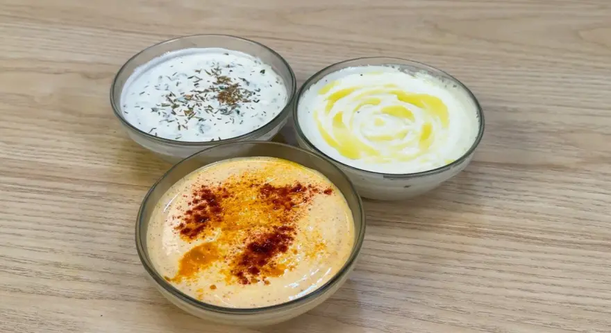 Tre ciotole di salsa con yogurt greco: una con erbe, una con olio d'oliva e una con paprika.