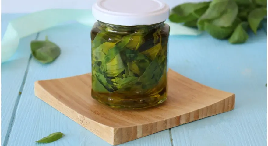 Un vasetto di basilico sott'olio, con foglie fresche sullo sfondo, pronto per insaporire i tuoi piatti.