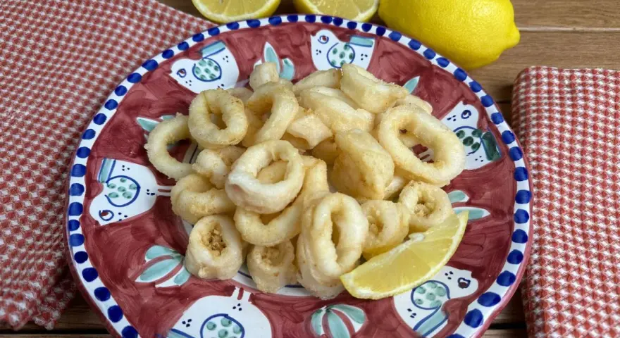 Un piatto di **calamari fritti** dorati, guarnito con spicchi di limone fresco, su un piatto decorato con uccelli stilizzati.