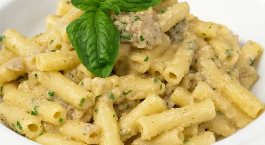 Un piatto di pasta con melanzane in bianco cremosa, condita con erbe aromatiche e guarnita con una foglia di basilico fresco.