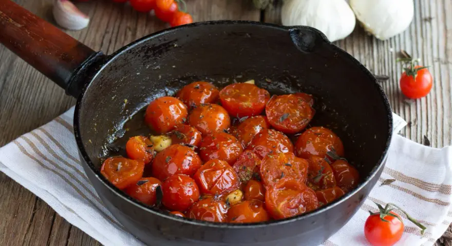 Pomodorini confit in padella, dolci e succosi, cotti con aglio e erbe aromatiche. Un contorno saporito e profumato.