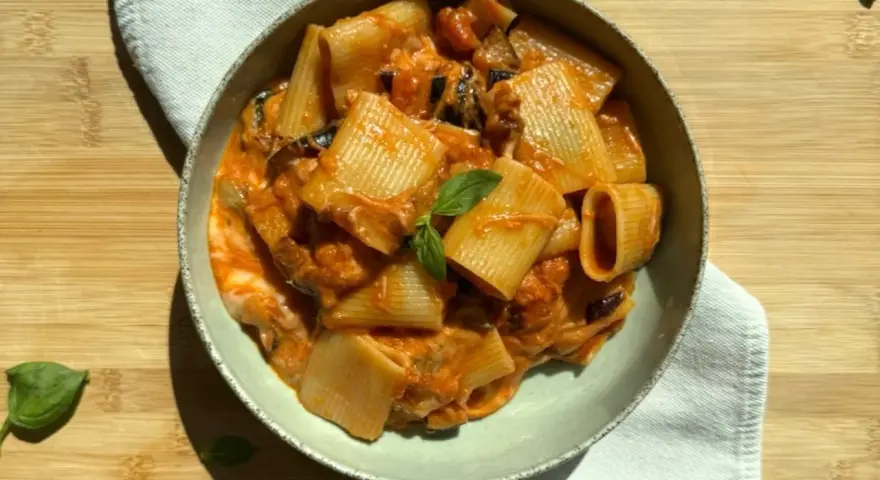 Un piatto di pasta alla siciliana con rigatoni, melanzane e una salsa cremosa al pomodoro, guarnito con basilico fresco.
