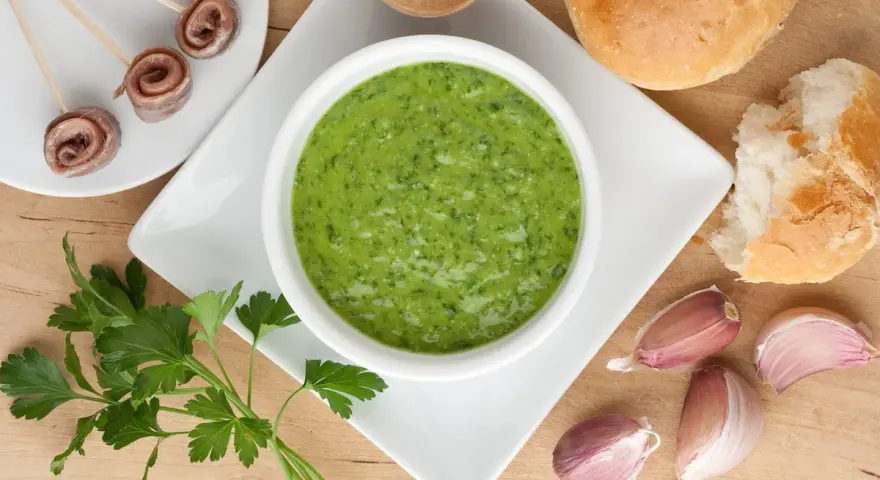 Un invitante bagnetto verde piemontese, accompagnato da acciughe arrotolate, pane fresco e spicchi d'aglio.