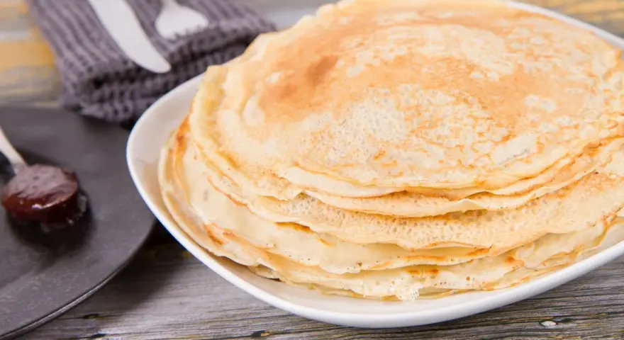 Pila di crepes senza uova, dorate e soffici, pronte per essere farcite. Accanto, un cucchiaino di marmellata.