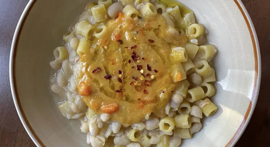 Un piatto di pasta e fagioli estiva, con ditalini e fagioli cannellini, guarnito con una purea di verdure e peperoncino.