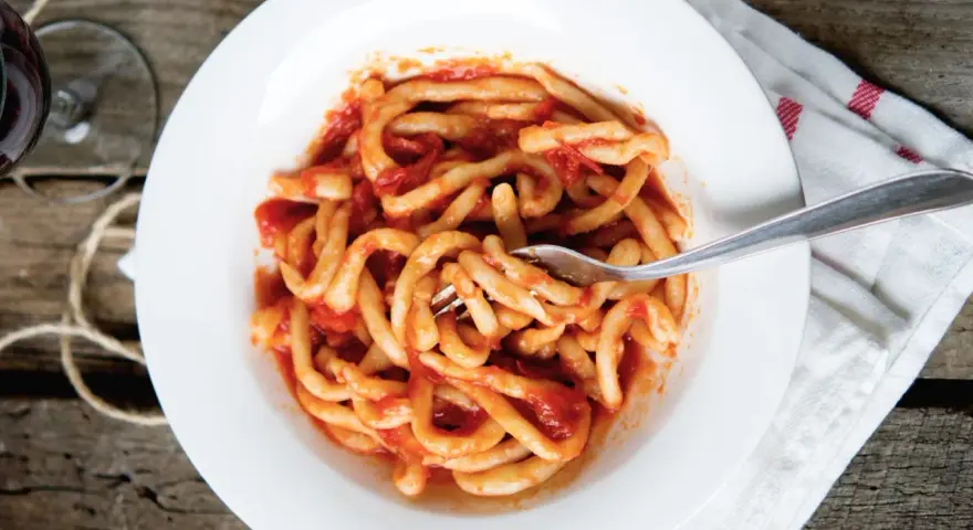 Piatto di pasta fresca condita con un saporito sugo all'aglione, servito su un piatto bianco con una forchetta.