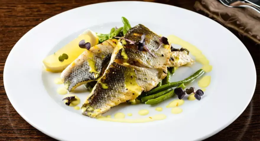 Deliziosi secondi di pesce con fagiolini croccanti, limone e una salsa gialla cremosa, guarniti con erbe viola.