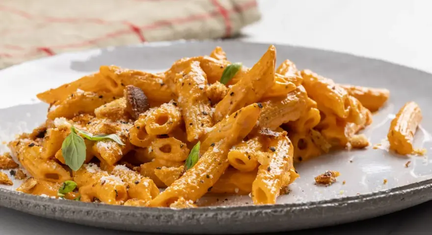 Penne con una ricca crema di peperoni, guarnite con basilico fresco e crostini croccanti. Un piatto invitante e saporito.