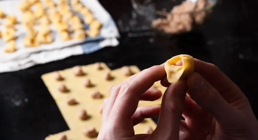Mani che creano tortellini fatti in casa, con la pasta fresca e il ripieno pronto.