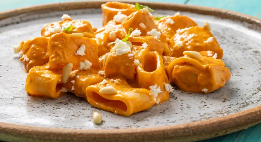 Paccheri cremosi con salsa arancione, formaggio sbriciolato e pinoli. Un piatto che ricorda il sapore del brodo vegetale Bimby.
