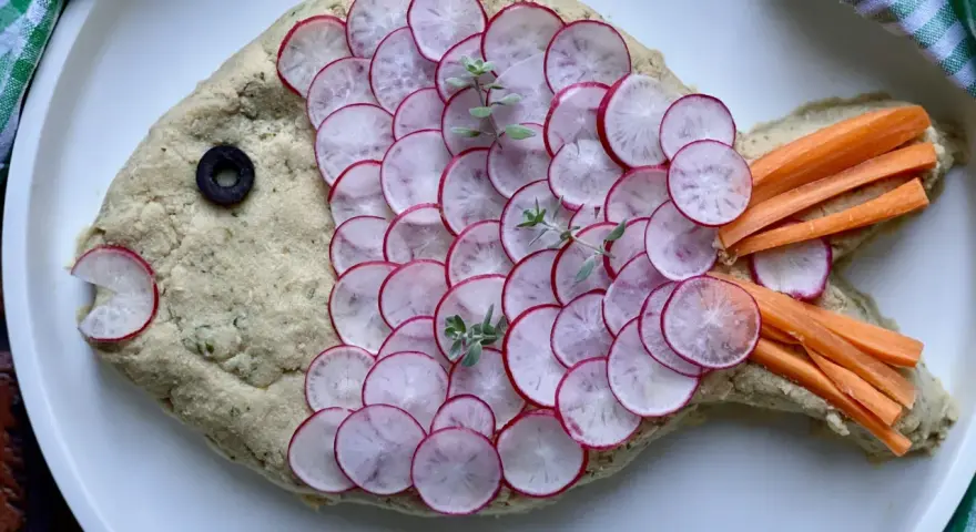 Pesce finto ricetta: un impasto cremoso decorato con ravanelli affettati, carote a bastoncino, un'oliva e erbe aromatiche.