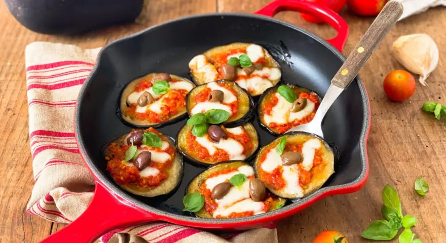 Melanzane in padella con pomodoro e mozzarella, guarnite con olive e basilico. Un antipasto invitante e saporito.