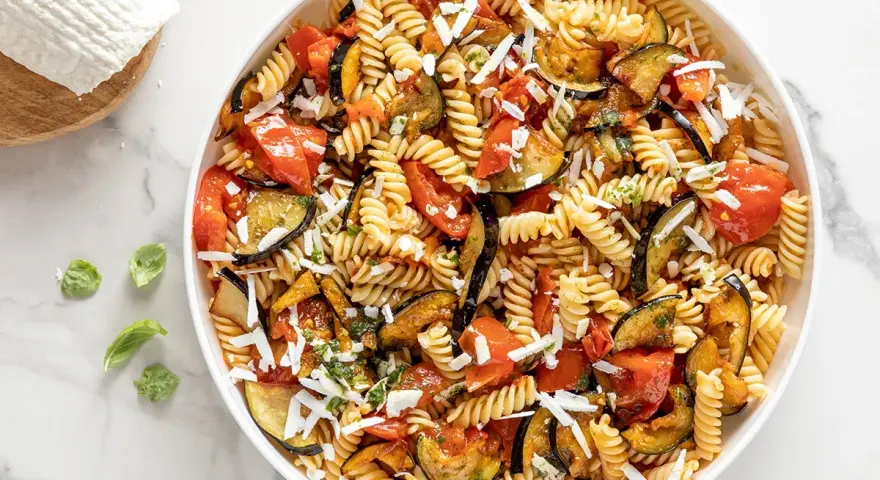 Un piatto invitante di pasta fredda alla norma con melanzane, pomodori e ricotta salata grattugiata.
