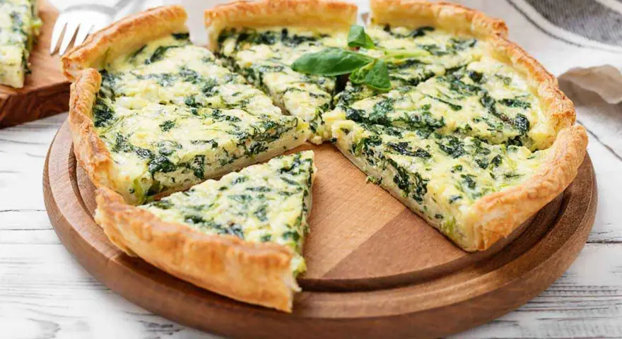 Una fetta di torta rustica ricotta e spinaci, con crosta dorata e ripieno cremoso, guarnita con basilico fresco.