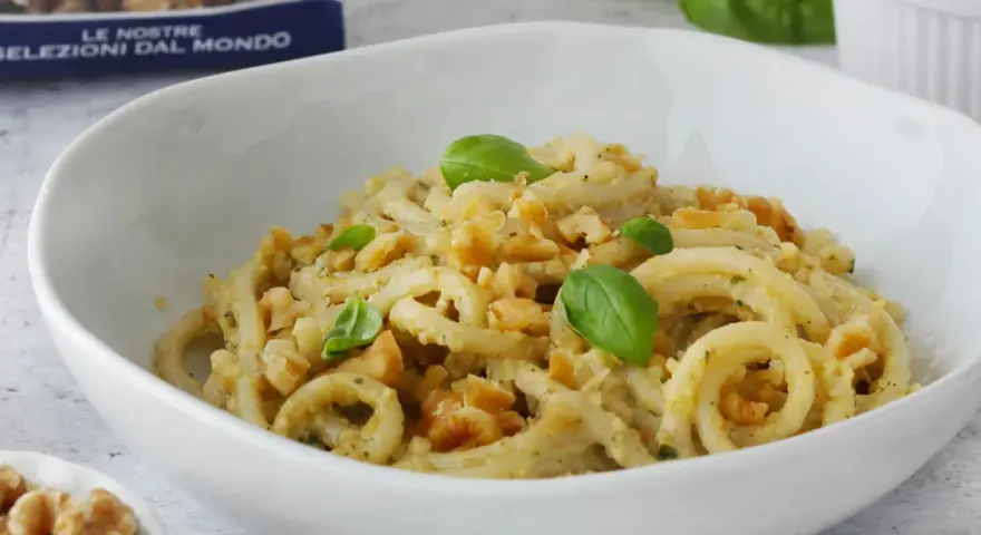 Pasta condita con un cremoso pesto di noci, guarnita con basilico fresco e noci croccanti.