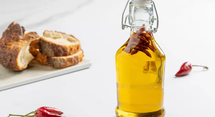 Olio al peperoncino in bottiglia, con pane rustico e peperoncini rossi. Un tocco piccante per ogni piatto.