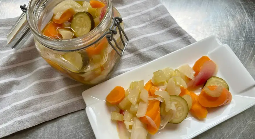 Giardiniera fatta in casa: carote, sedano, cipolle e cetrioli sottaceto in un barattolo e su un piatto. Ricetta facile e gustosa.