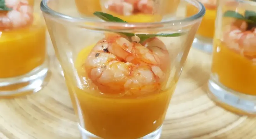 Deliziosi finger food gamberi su crema arancione in bicchierini, guarniti con menta.