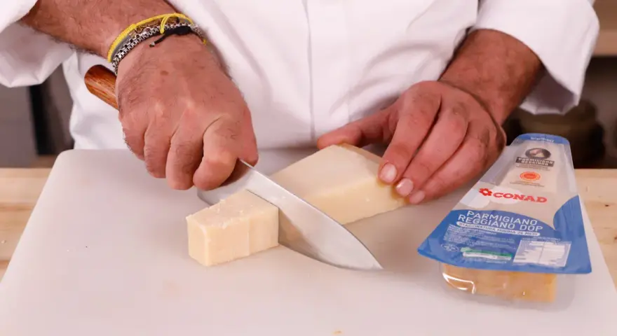 Mani che tagliano un pezzo di Parmigiano Reggiano, pronto per una deliziosa fonduta.