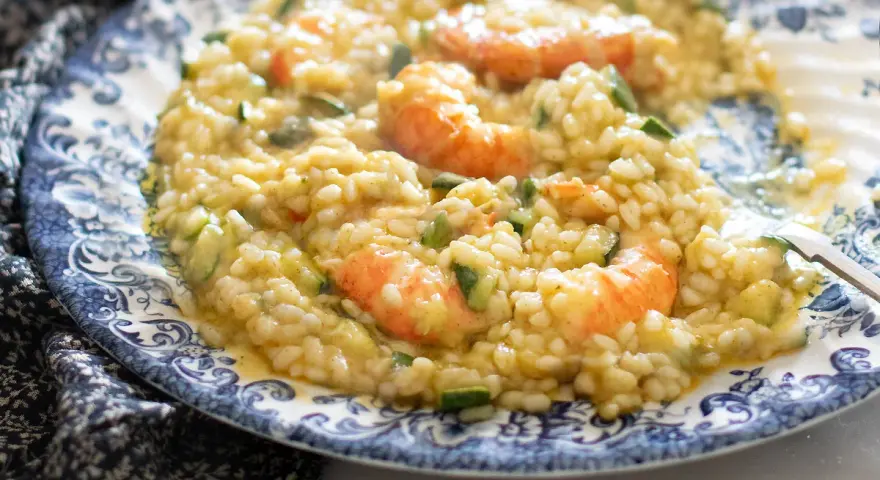 Un cremoso risotto zucchine e gamberetti, servito su un piatto decorato.