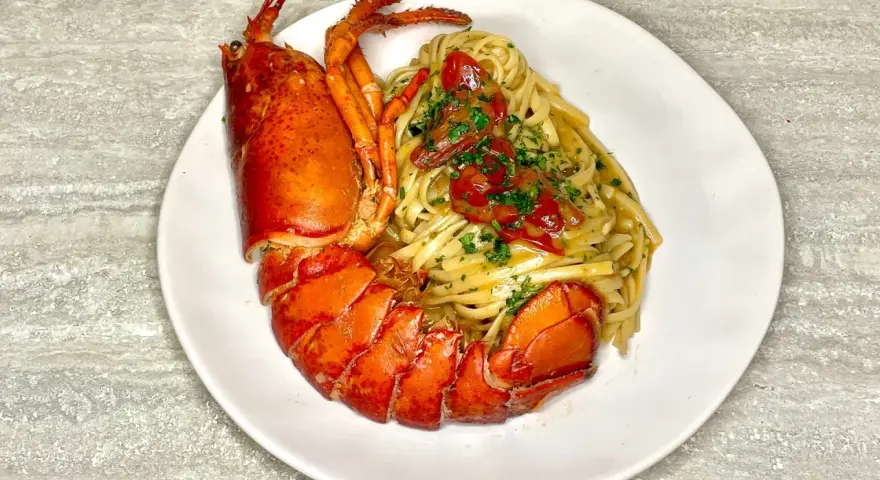 Un piatto di linguine all'astice, con pasta condita e astice intero, guarnito con pomodorini e prezzemolo.