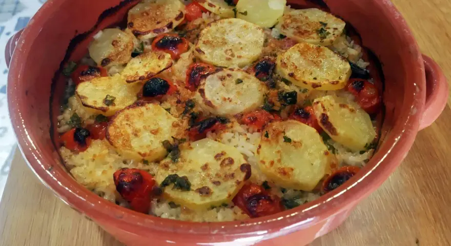 Piatto di riso patate e cozze cotto al forno, con pomodorini e erbe aromatiche, servito in una terrina di terracotta.