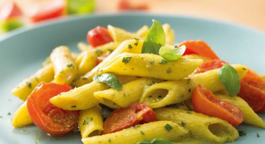 Penne al pesto con pomodorini freschi e basilico, un piatto colorato e saporito.