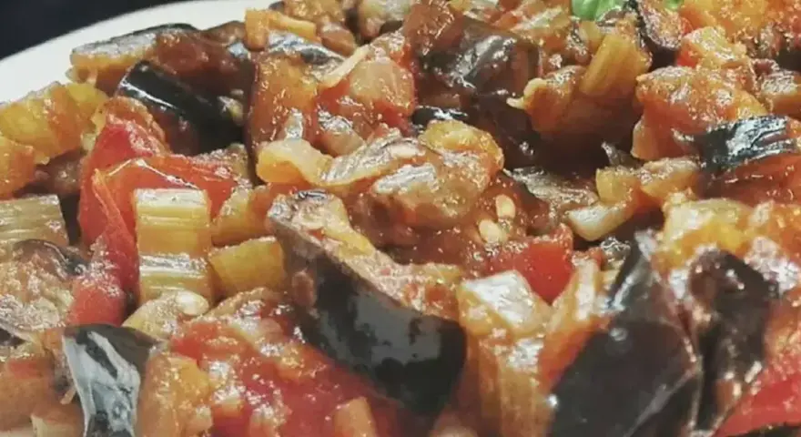 Un primo piano di una saporita caponata siciliana, con melanzane, pomodori e sedano cotti a puntino.