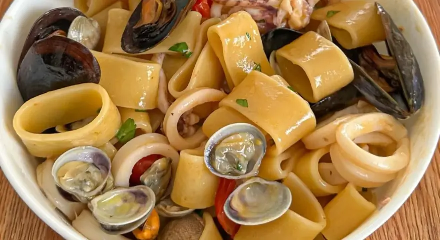 Calamarata allo scoglio ricca di cozze, vongole e anelli di calamaro, un piatto di mare invitante.