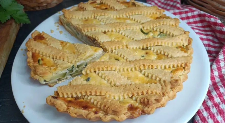 Una deliziosa crostata salata con zucchine e formaggio, con una griglia di pasta dorata e un pezzo tagliato.