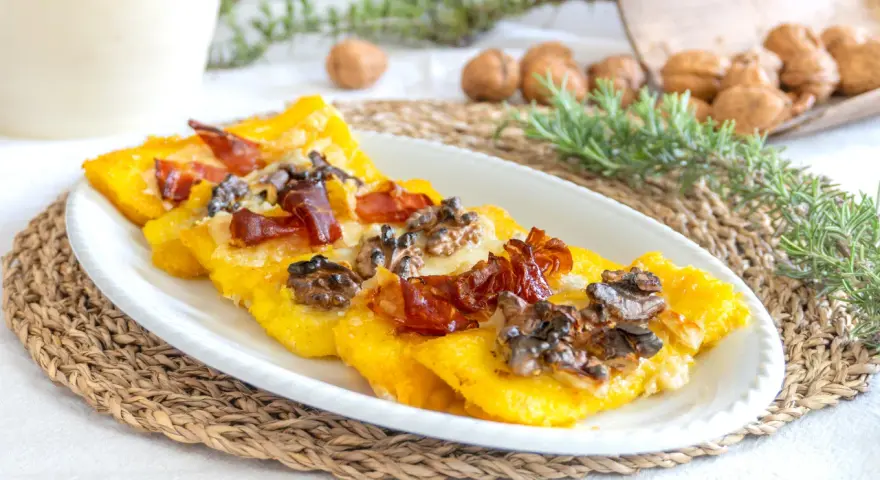 Deliziosi crostini di polenta freddi con prosciutto croccante e noci, un antipasto rustico e saporito.