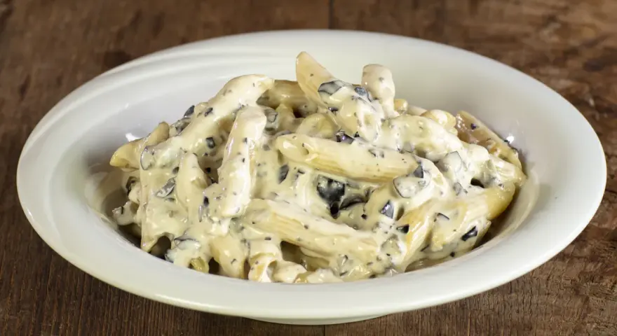 Penne cremose con pezzetti scuri, un piatto invitante di pasta alla cenere, servito in una ciotola bianca su un tavolo di legno rustico.